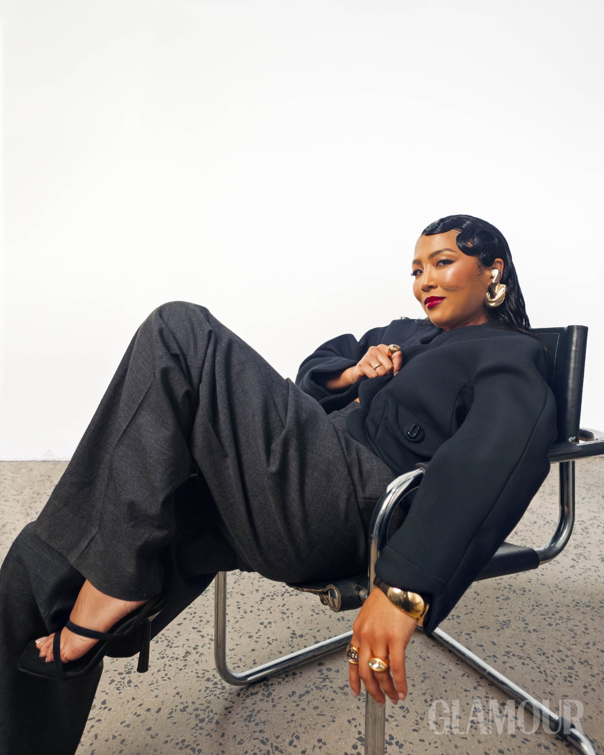 Chanley Wong in black tailoring reclining in a chrome chair